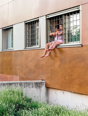 Niños se asoman en una ventana con rejas